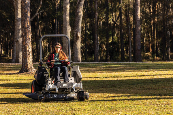 Vooraanzicht van de Bobcat ZT6000 zero-turn maaier met een vrouwelijke bestuurder met zonnebril en hoofdtelefoon die het gras maait.