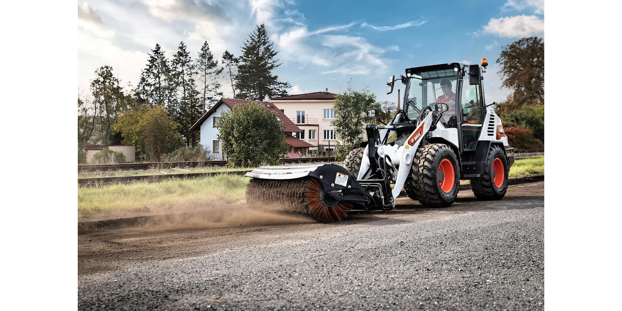 Bobcat compacte wiellader met veegmachine aan het werk op een weg