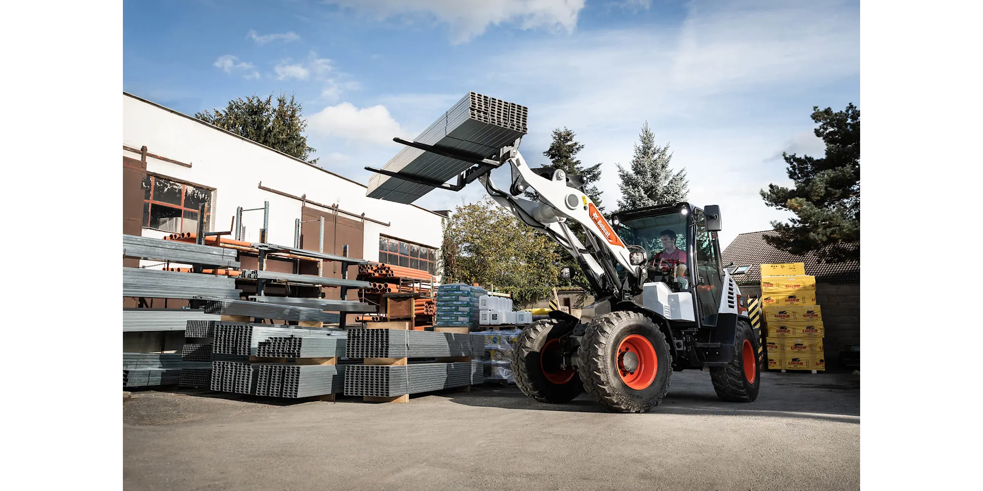 Bobcat compacte wiellader met palletvorken laadt stalen balken bij een bouwmaterialenhandel