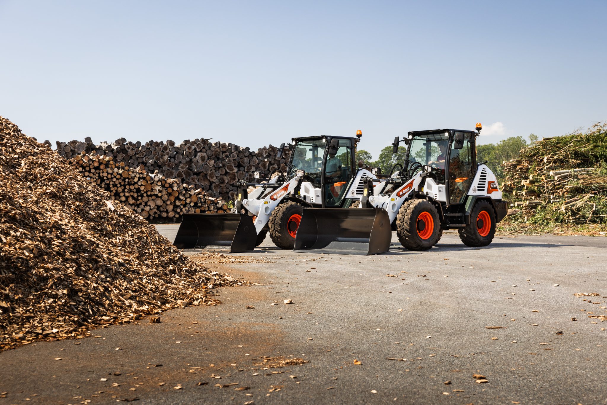 Bobcat L85 en Bobcat L100 compacte wielladers naast elkaar met bak en houtsnippers en boomstammen
